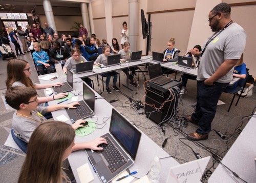 a man teaches a group of children at computers